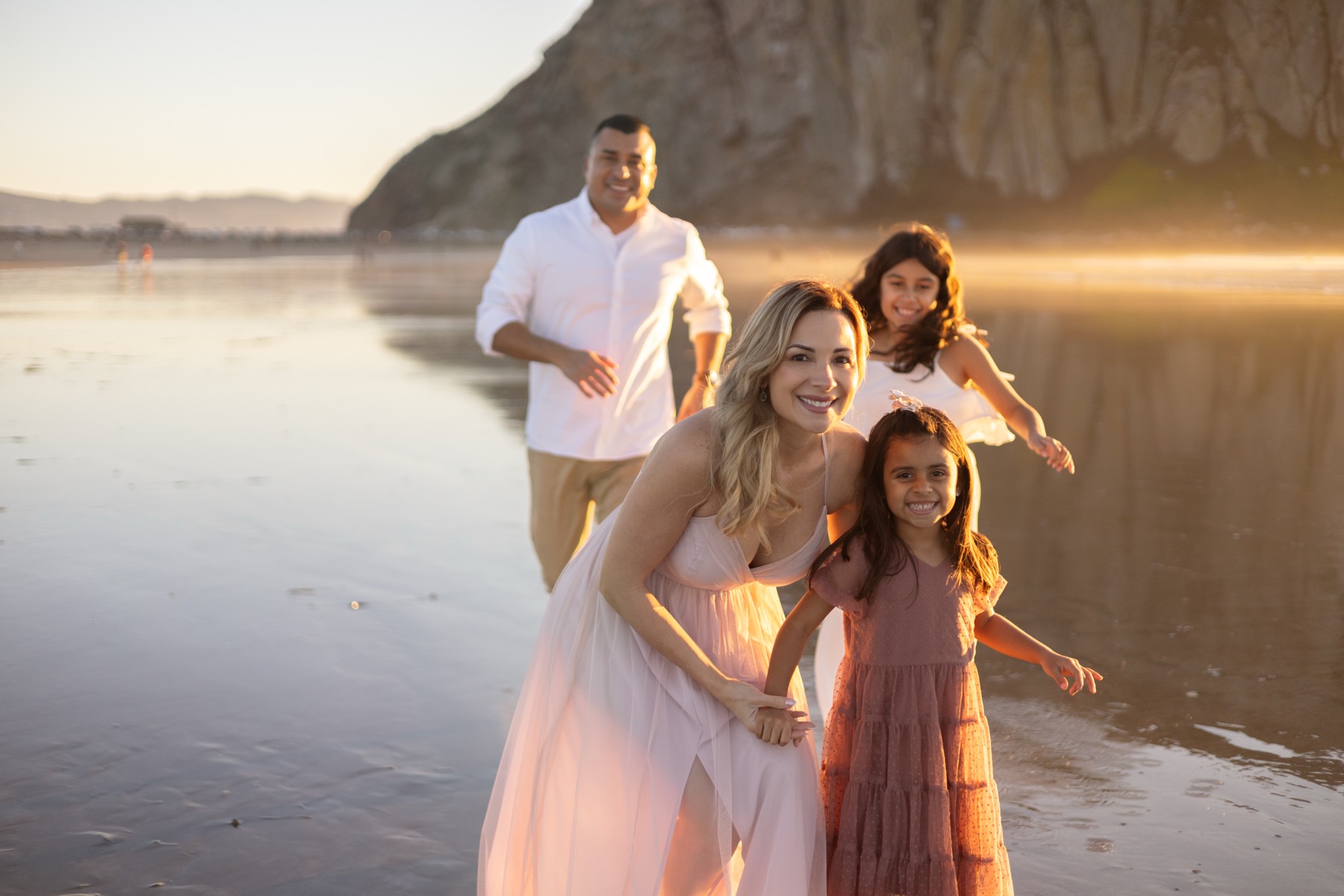 Mom and daughters smiling on the beach with dad behind