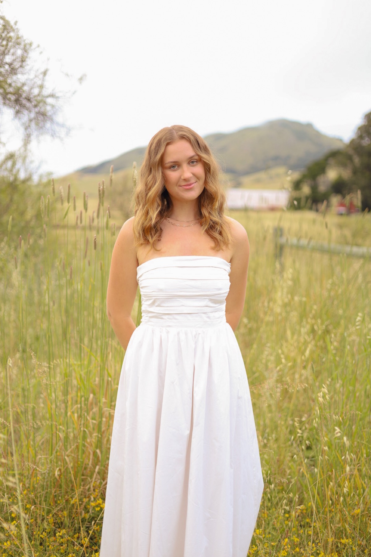 Portrait in a white dress in a grassy field below the hills