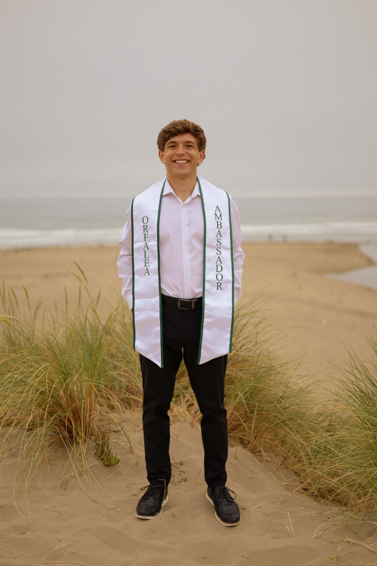 Graduate in a white shirt and stole on the beach dunes