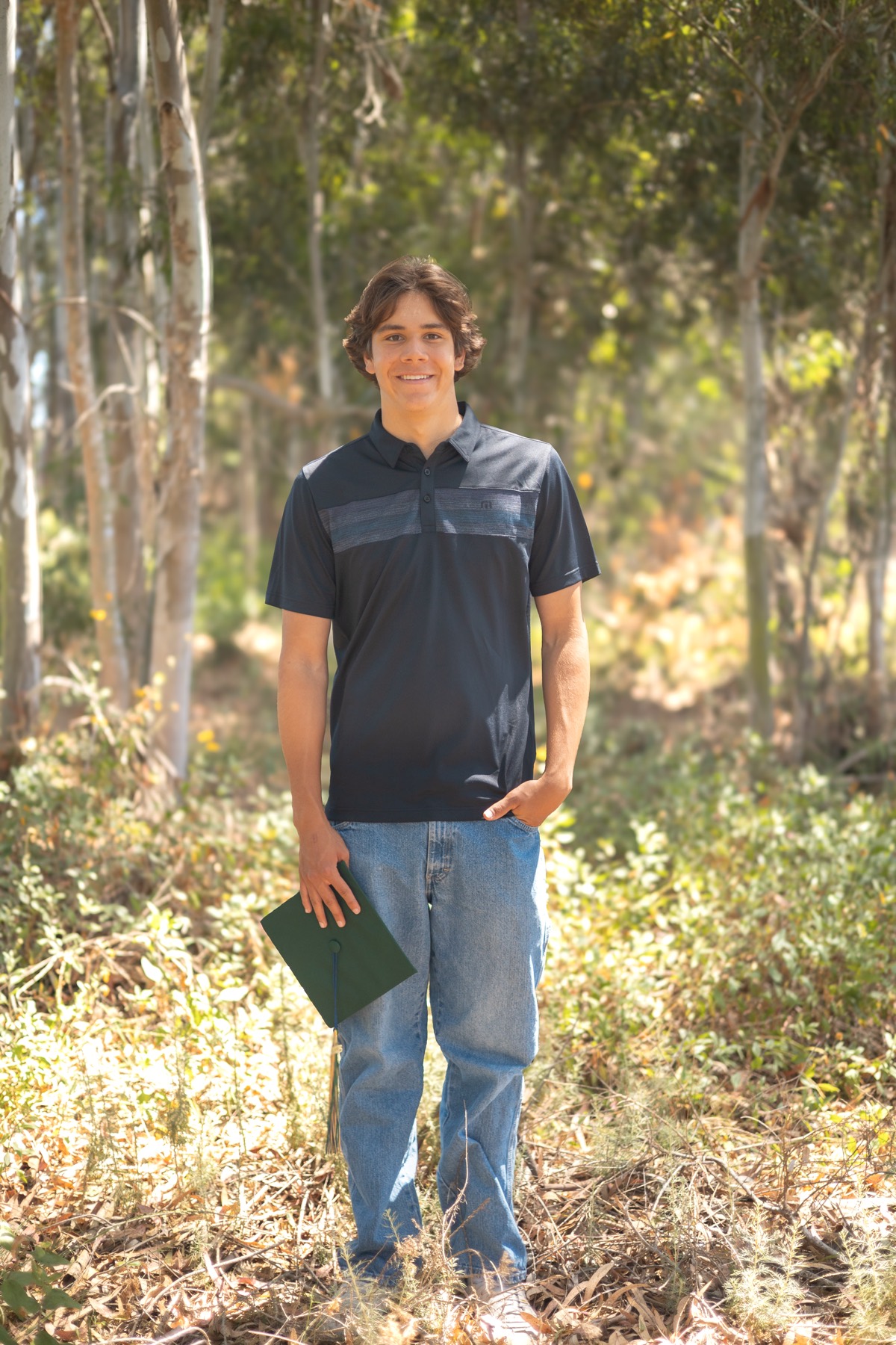 Senior portrait in the woods holding his diploma cover