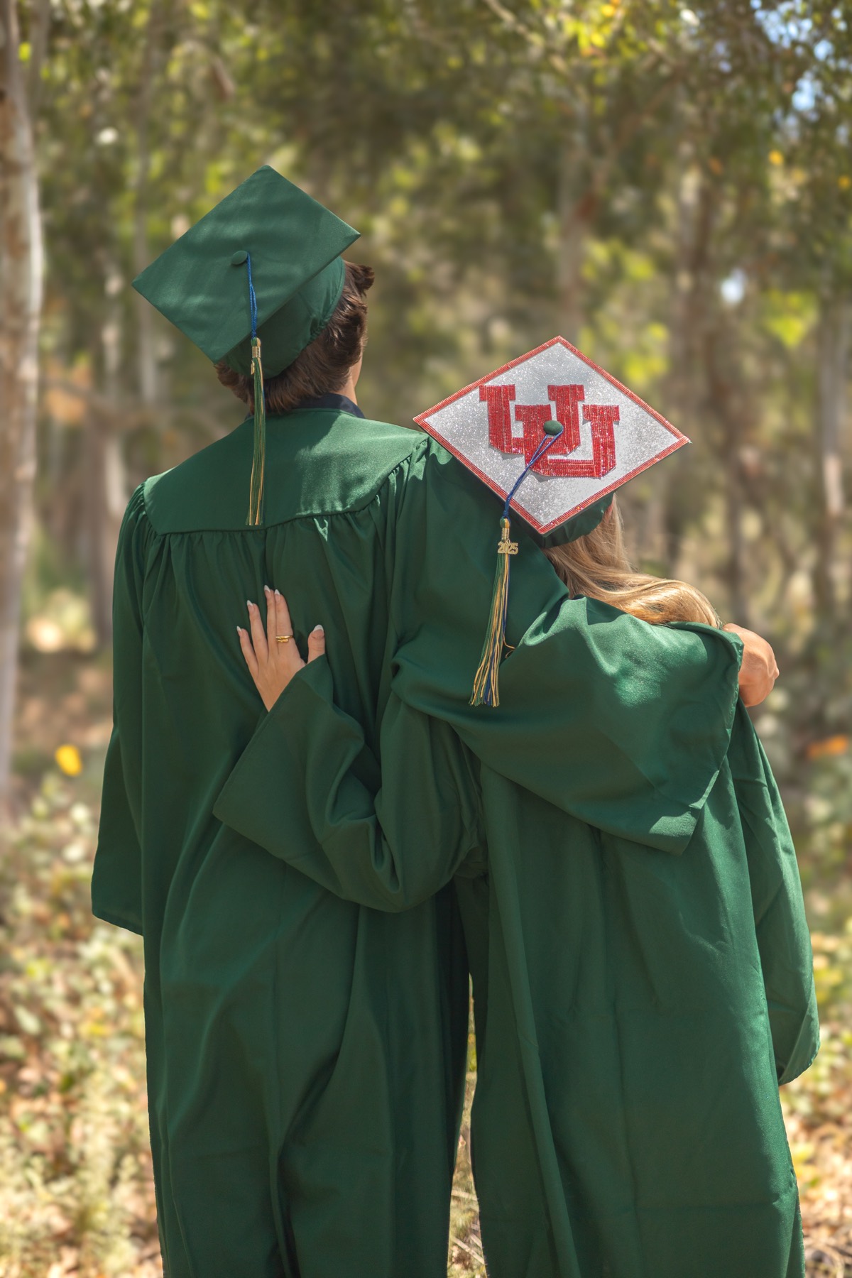 Two graduates in caps and gowns, seen from behind, arm in arm