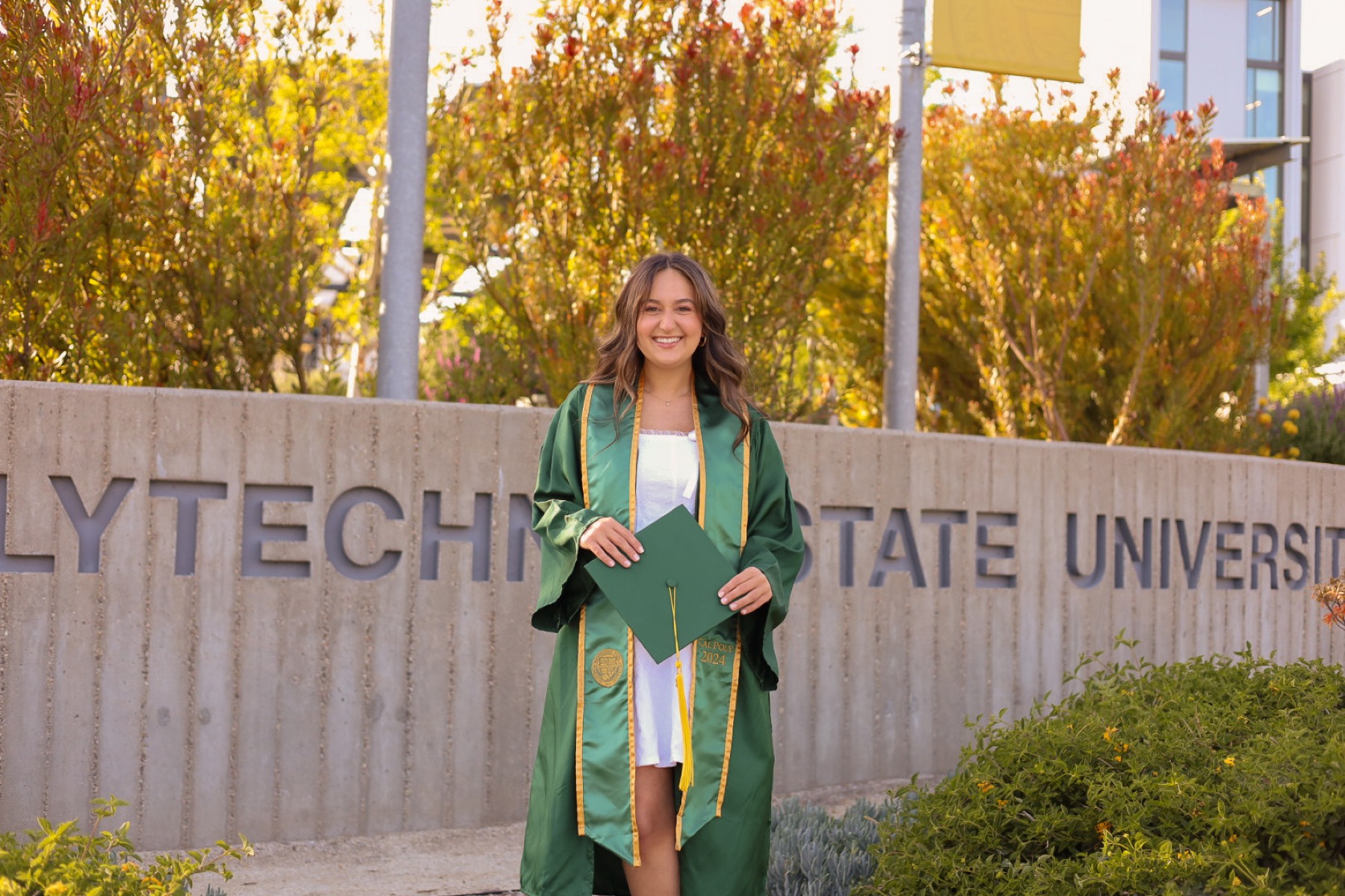 Graduate in a green stole by the Cal Poly university sign